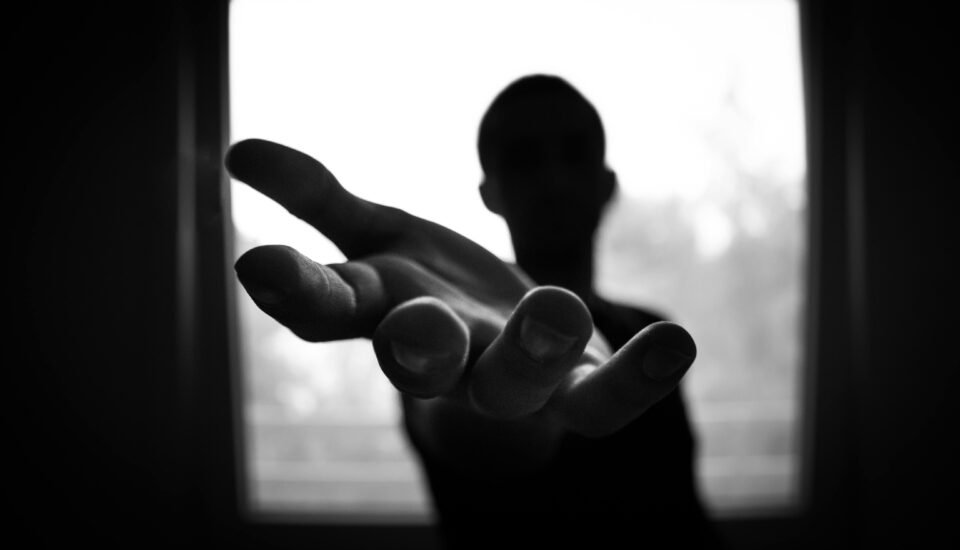Silhouette of a hand reaching out in a black and white contrast.